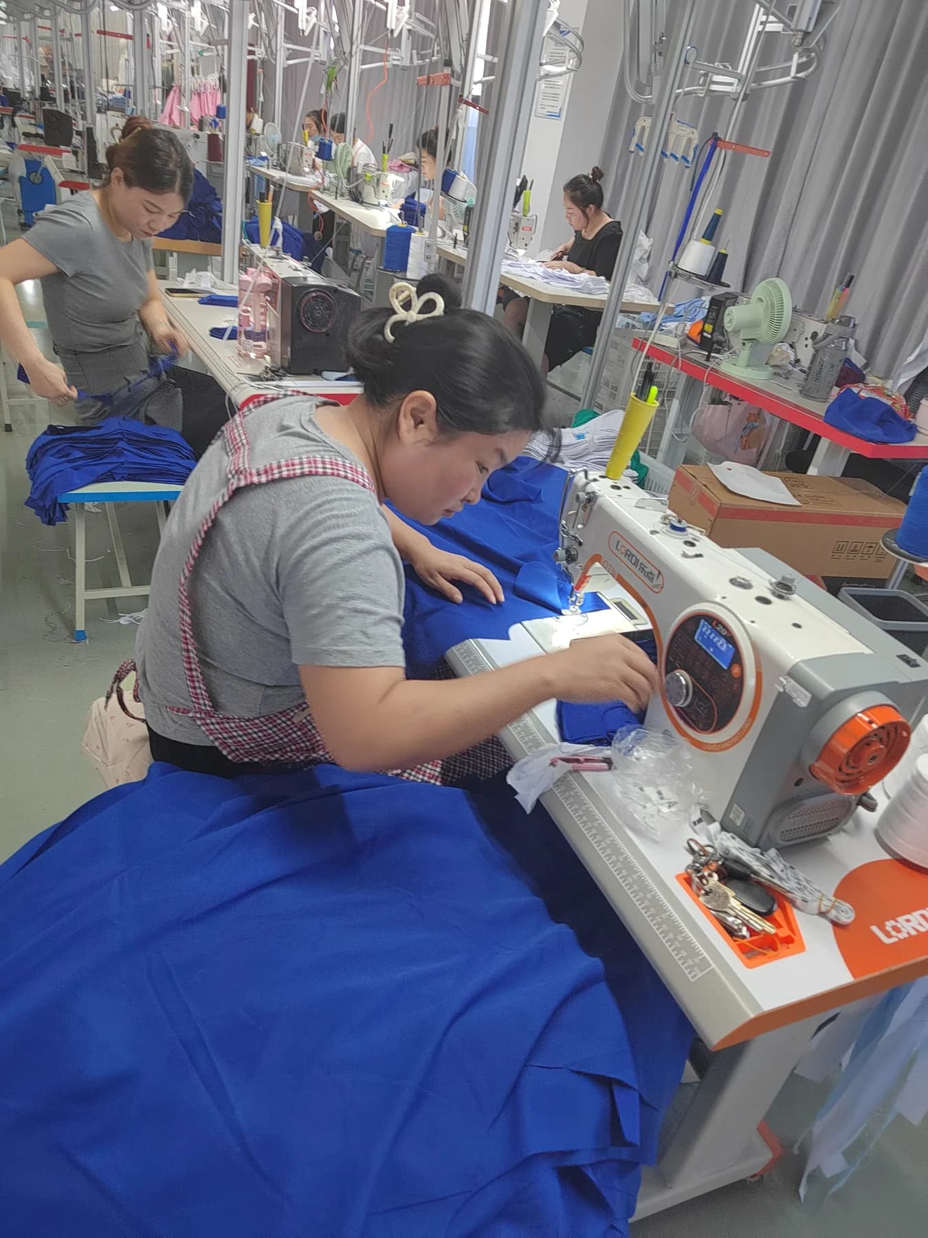 Operator sewing blue garment panels at a medical uniform workshop sewing station