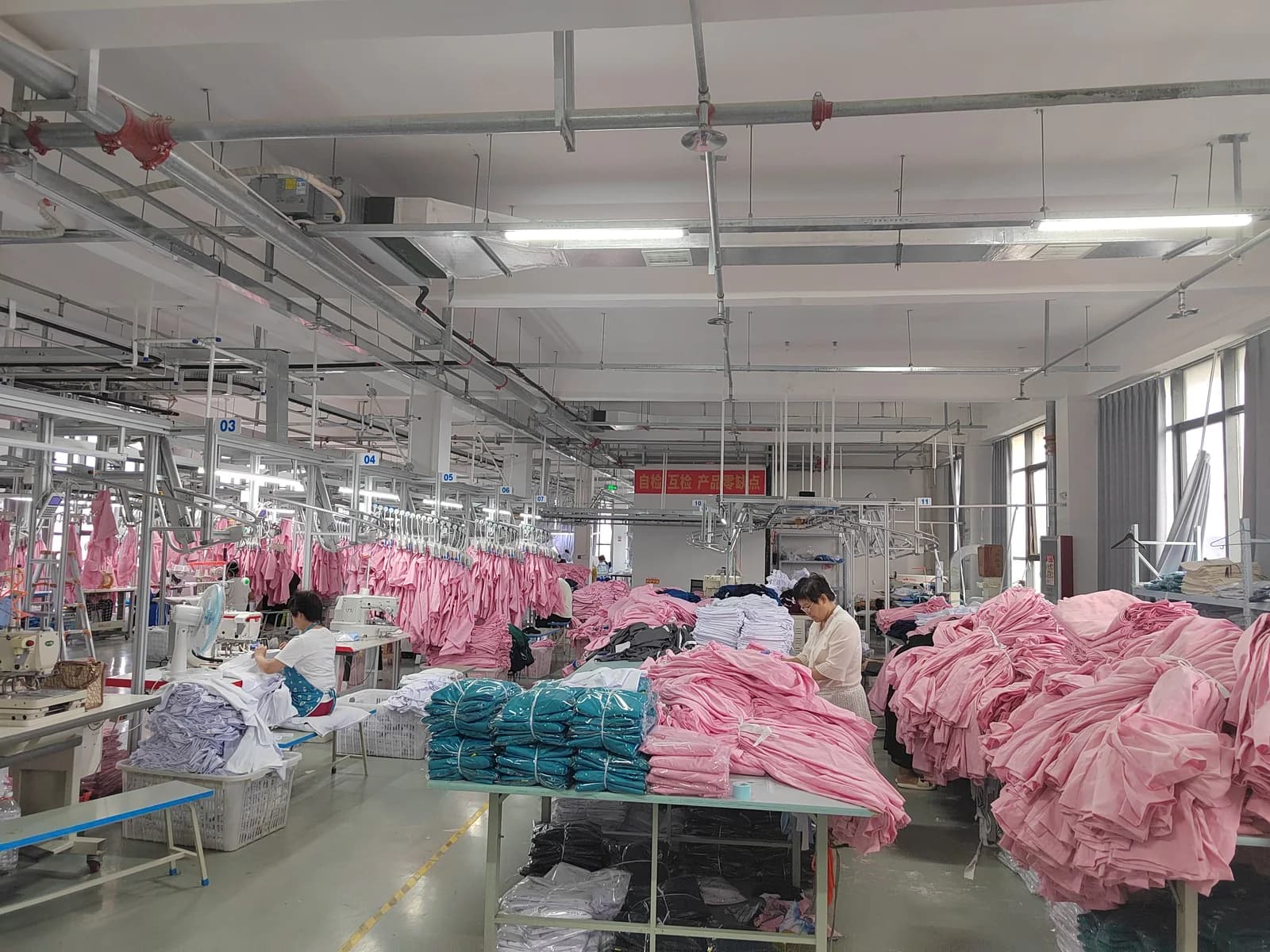 Medical uniform workshop with sewing stations, pink uniforms and packed garments
